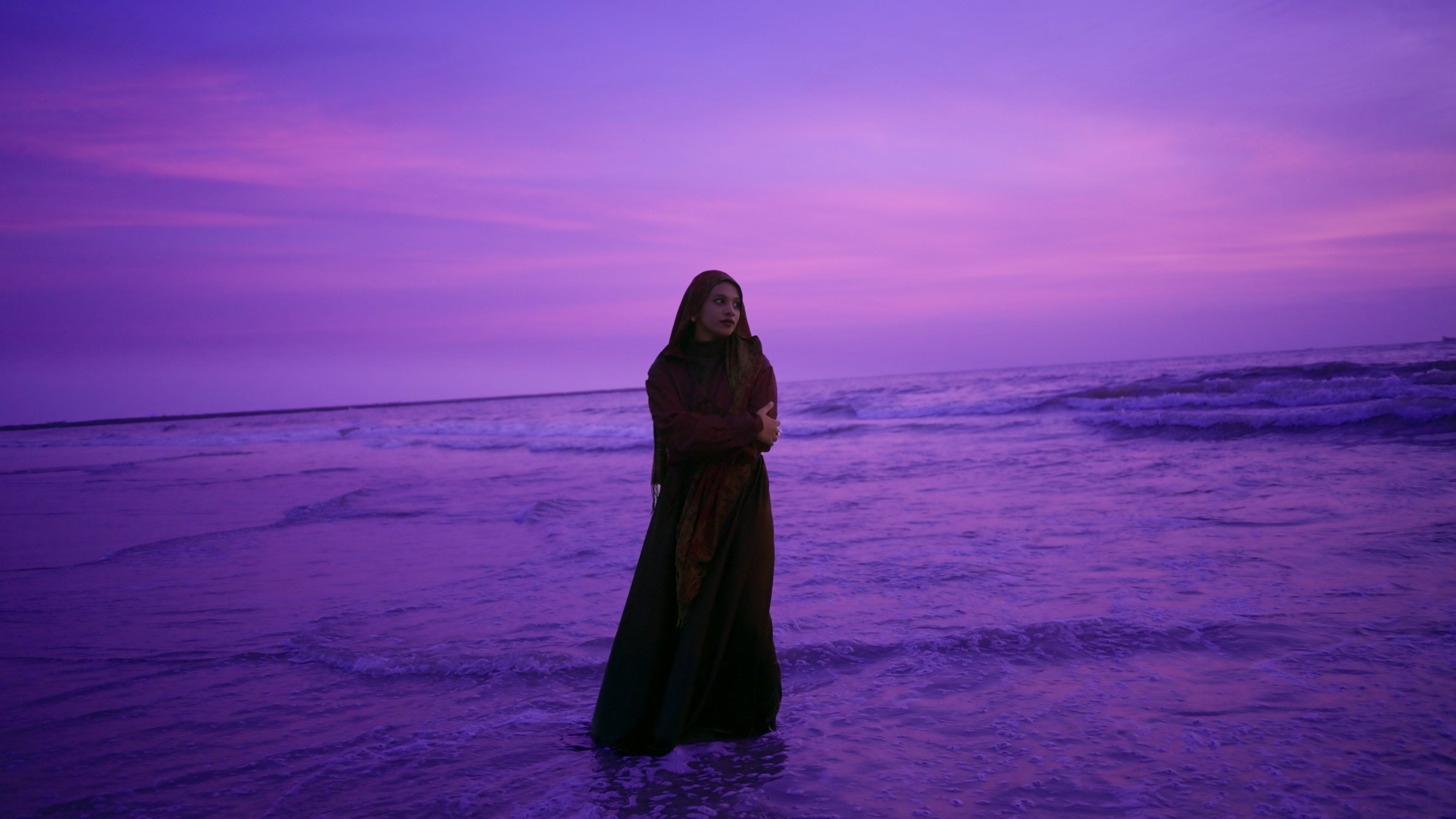 The same frame graded: a deep violet and magenta dusk sky and sea, with her face and shawl kept warm and natural.