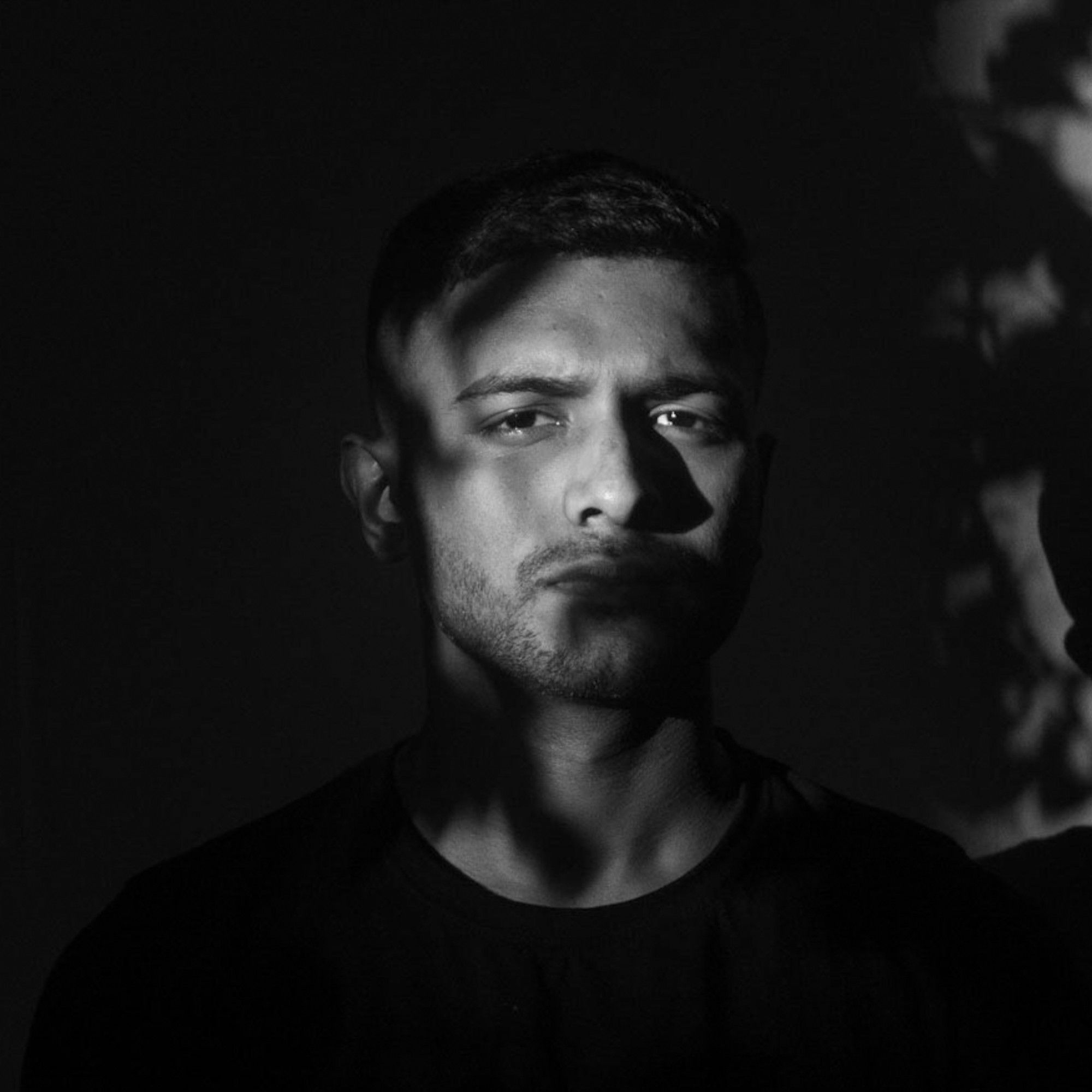 Black-and-white portrait of Masru in low light, with leaf shadows falling across the face.